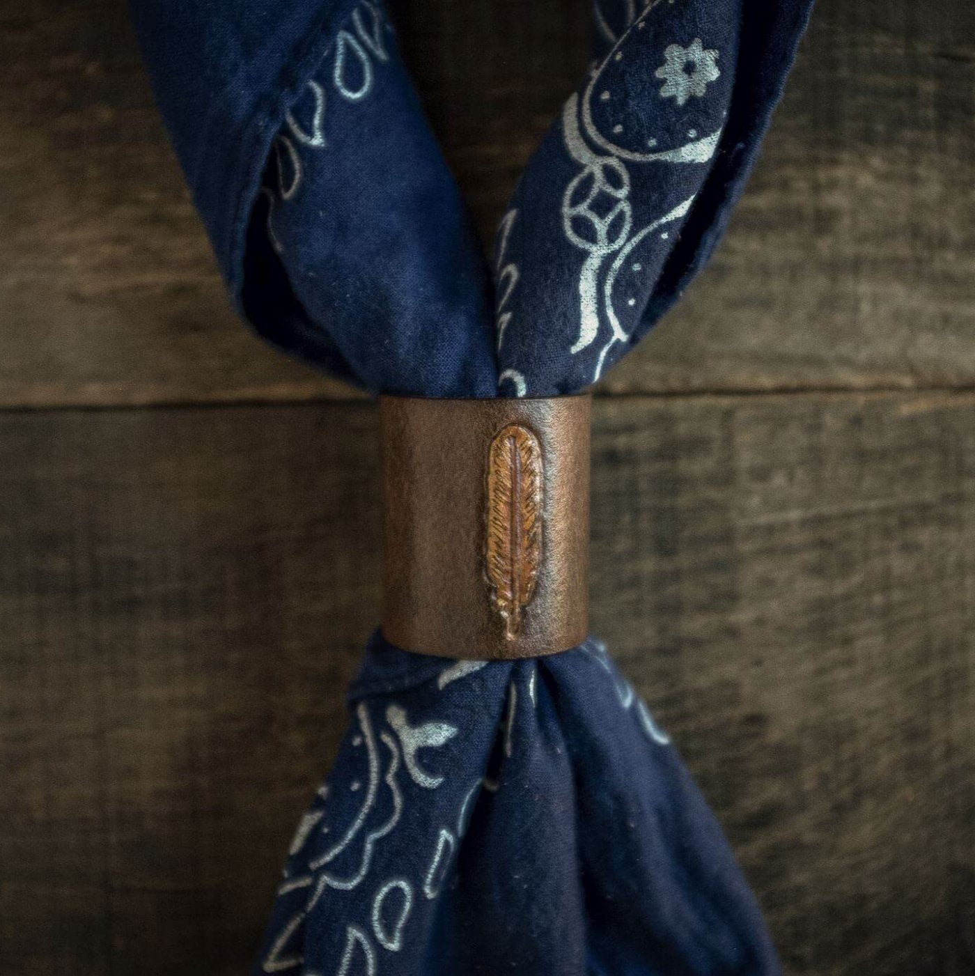 Woggle, bandana / neckerchief slide made from leather with a feather image stamp, around a blue bandana