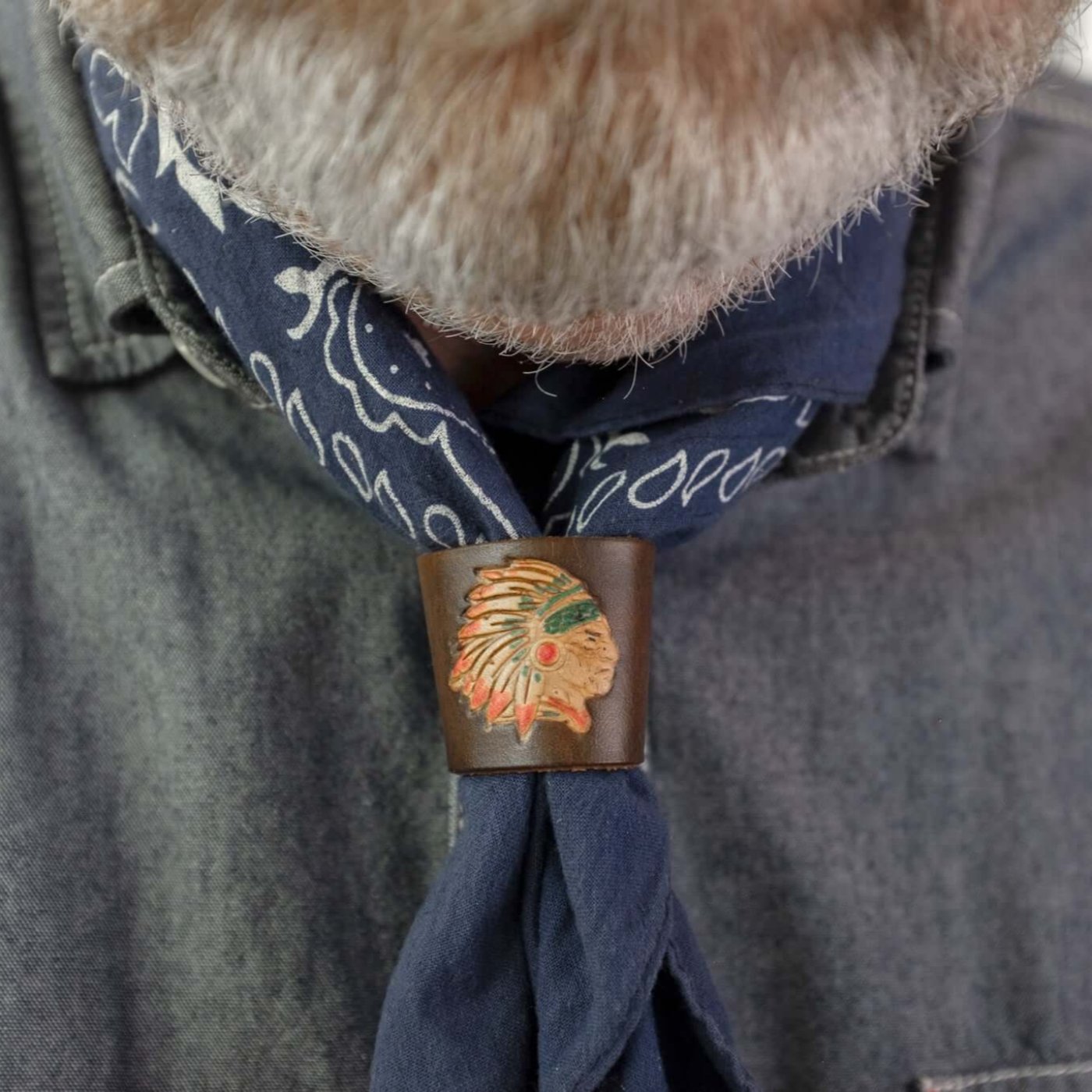 Woggle, bandana / neckerchief slide made from brown leather with an Indian Chief image stamp, wearing around a blue bandana