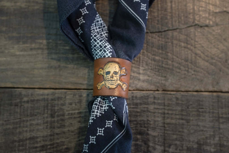 Woggle, bandana / neckerchief slide in cognac leather with a skull image stamp, around a blue bandana