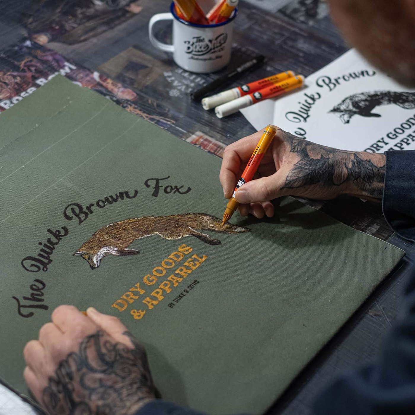 hand drawing The Quick Brown Fox logo on the olive green canvas tote bag