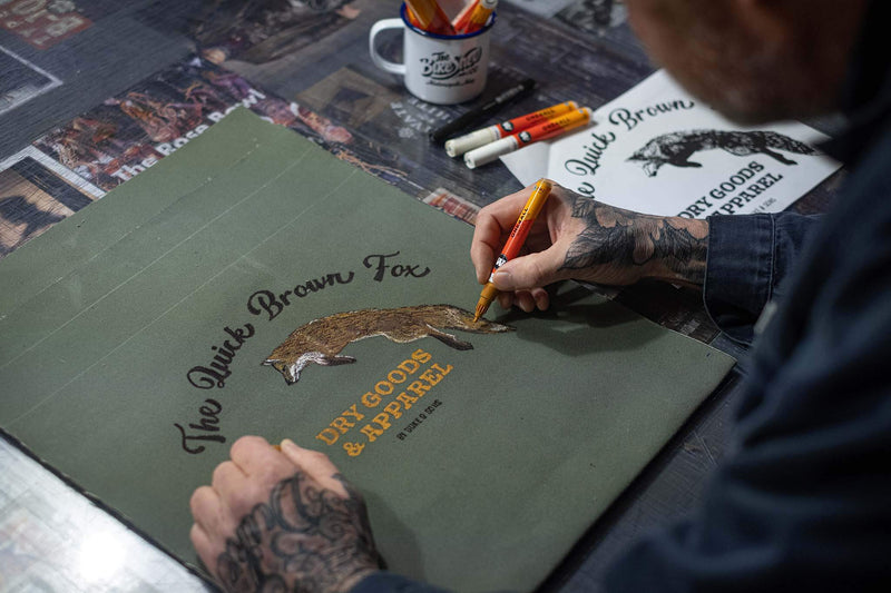 hand drawing The Quick Brown Fox logo on the olive green canvas tote bag