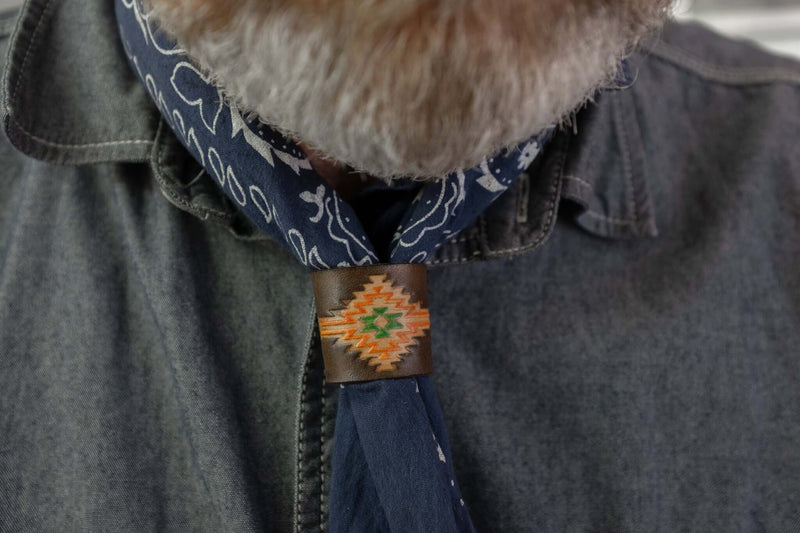 Woggle, bandana / neckerchief slide in brown leather with a rectangle native pattern stamp, wearing around a blue bandana