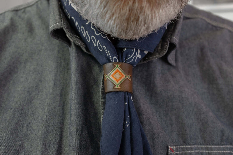 Woggle, bandana / neckerchief slide in brown leather with a square native pattern stamp, wearing around a blue bandana
