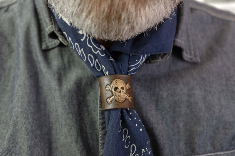 Woggle, bandana / neckerchief slide in brown leather with a skull image stamp, wearing around a blue bandana
