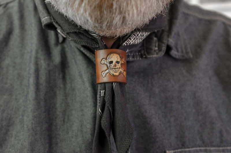Woggle, bandana / neckerchief slide in cognac leather with a skull image stamp, wearing around a blue bandana